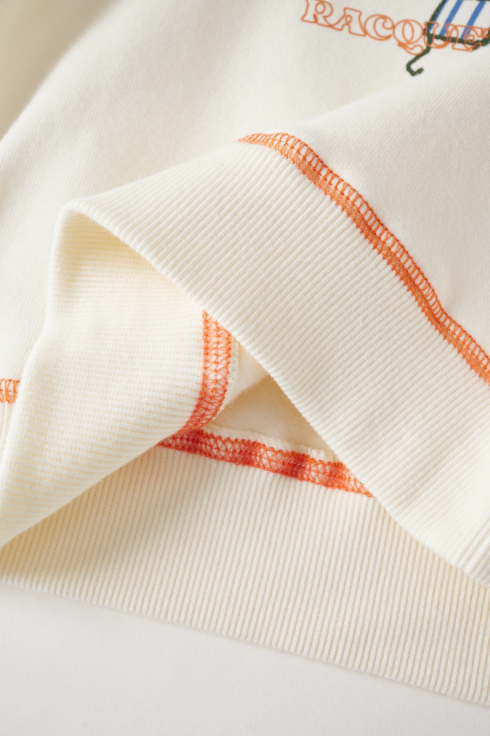 Close-up of a white garment with orange stitching on a light background