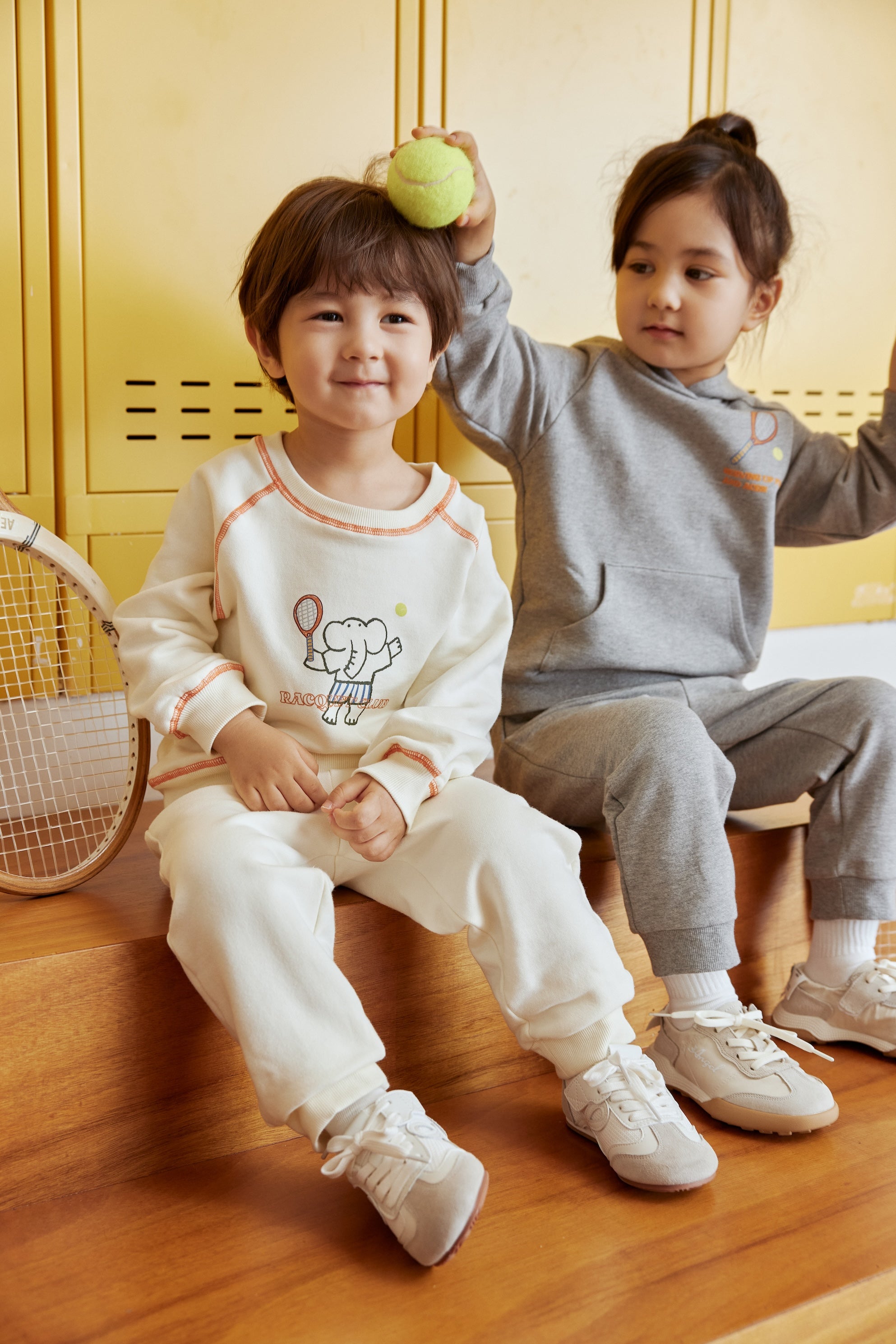 Two children sitting on a wooden floor with a yellow locker in the background.