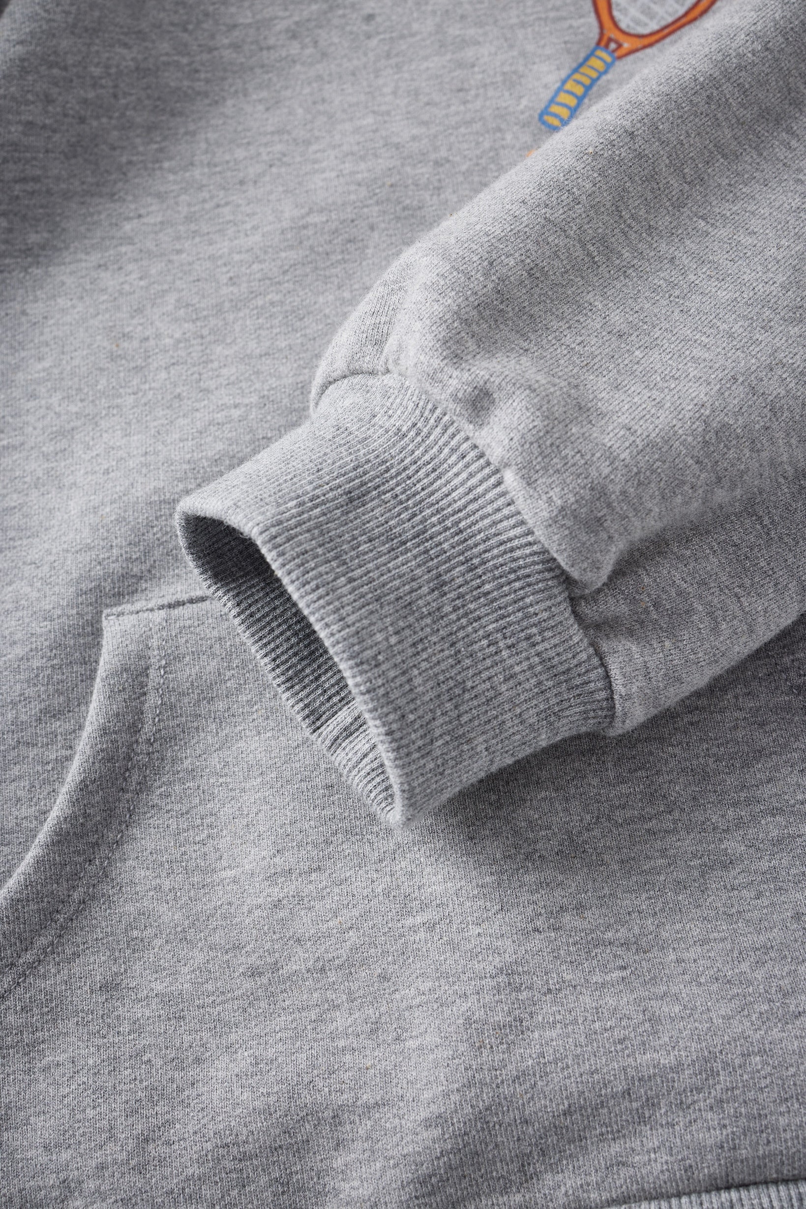 Close-up of a gray sweatshirt with a brand logo on the sleeve.
