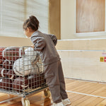 Child pushing a cart full of basketballs in an indoor setting with an emergency exit sign visible.