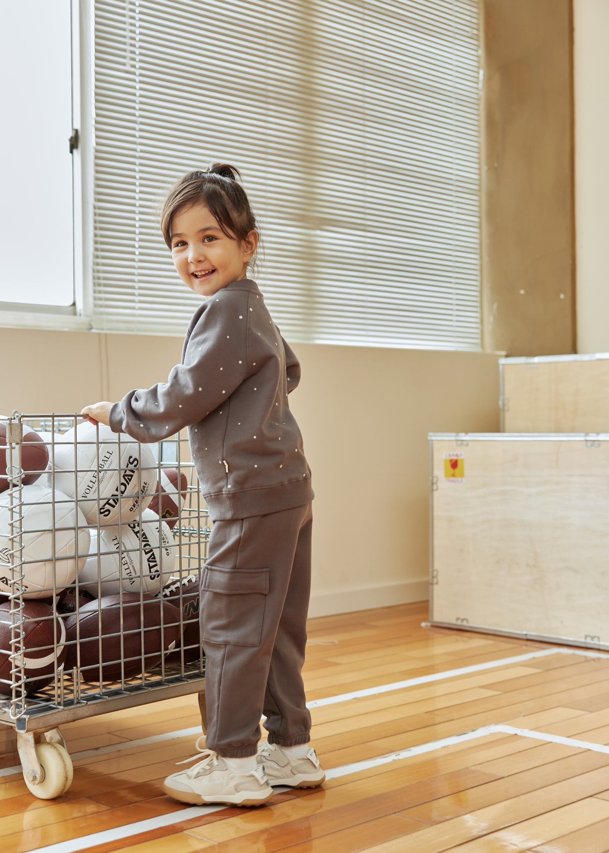 Child pushing a cart with sports balls in a gymnasium
