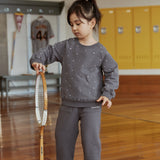 Child in a gray outfit holding a tennis racket in an indoor setting with lockers.