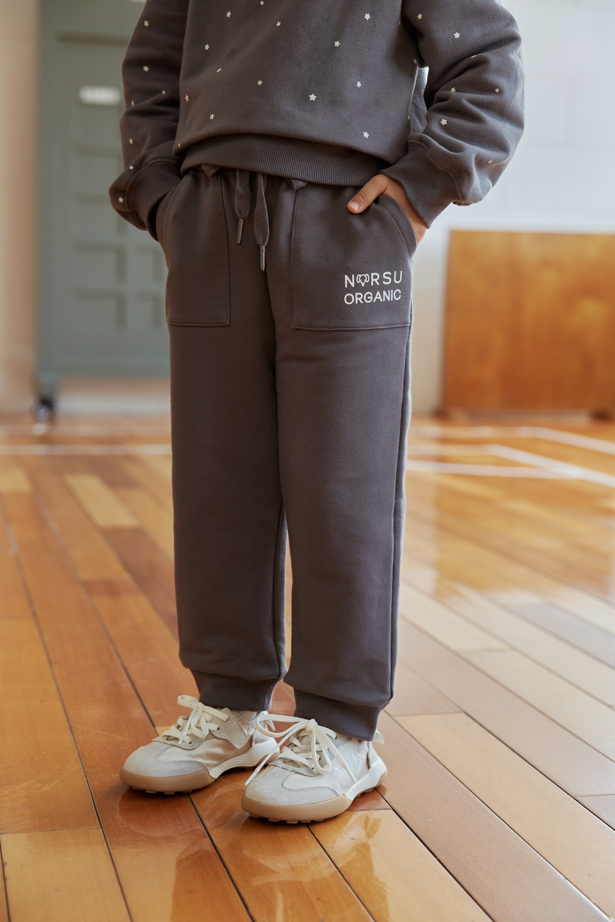 Person wearing a gray tracksuit with 'NORSU ORGANIC' branding on a wooden floor.