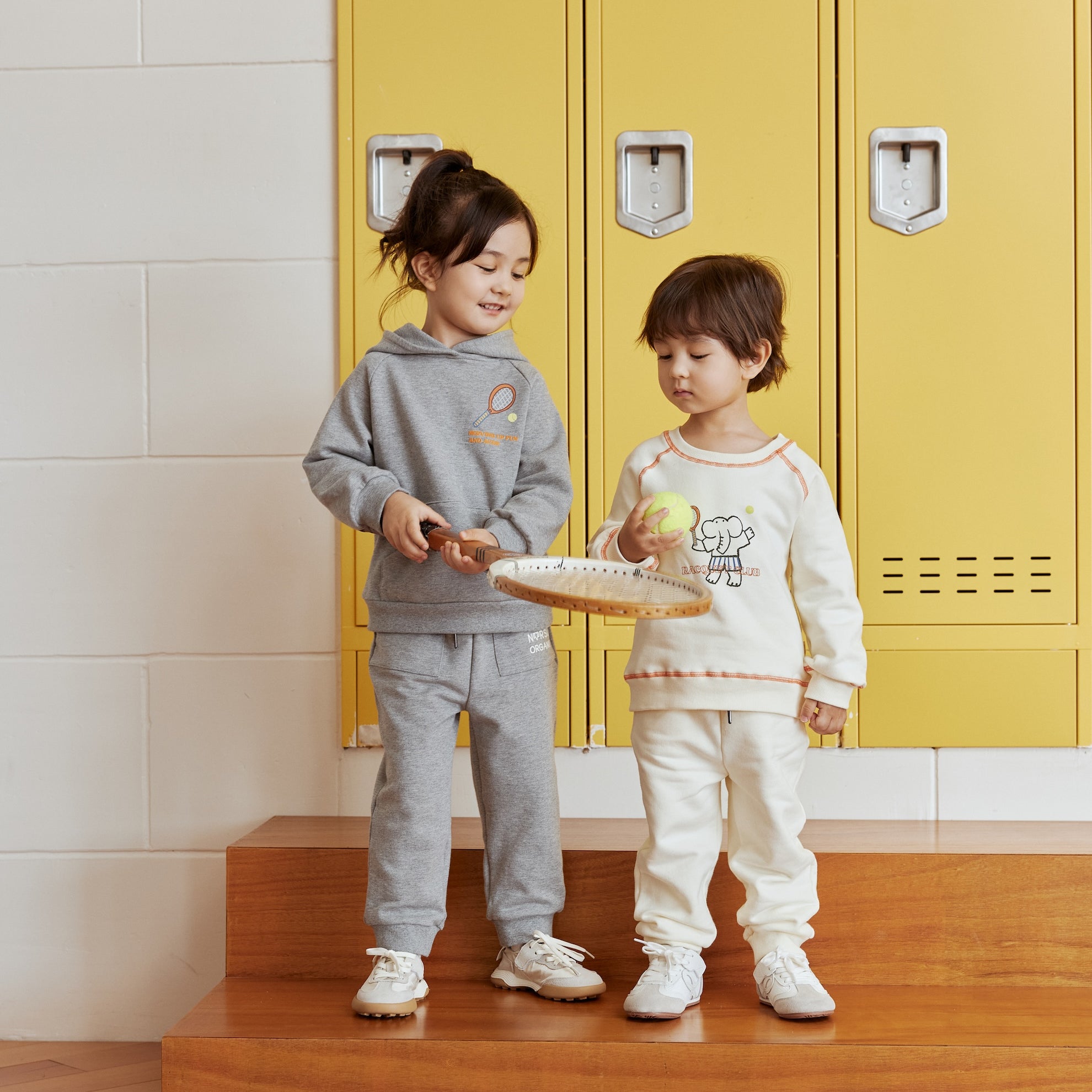 Two children standing on wooden steps in front of yellow lockers with a warning sign above.