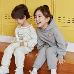 Two children sitting on a wooden floor in front of yellow lockers, wearing matching outfits.