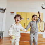 Two children playing with a tennis ball and racket in an indoor setting with yellow lockers.