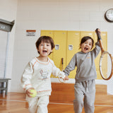 Two children playing with a tennis ball and racket in an indoor setting with yellow lockers.