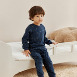 Child wearing a navy blue outfit with hockey pattern sitting on a white couch.