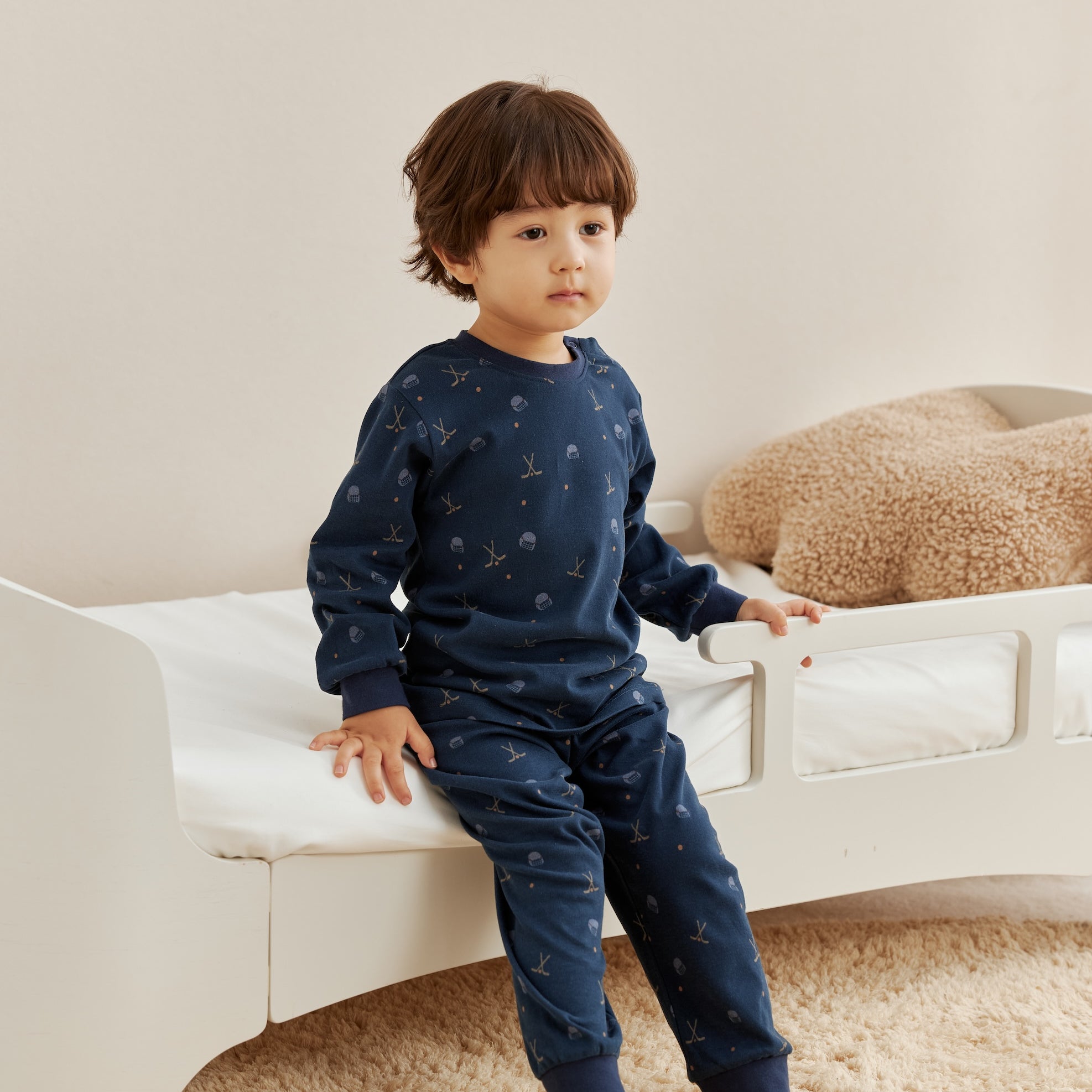 Child wearing a navy blue outfit with hockey pattern sitting on a white couch.
