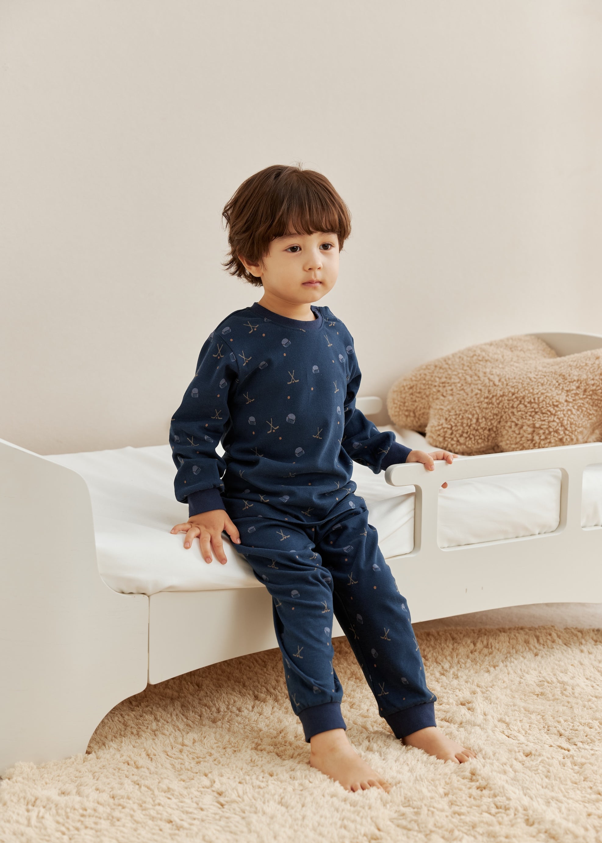 Child wearing a navy blue outfit with hockey pattern sitting on a white couch.