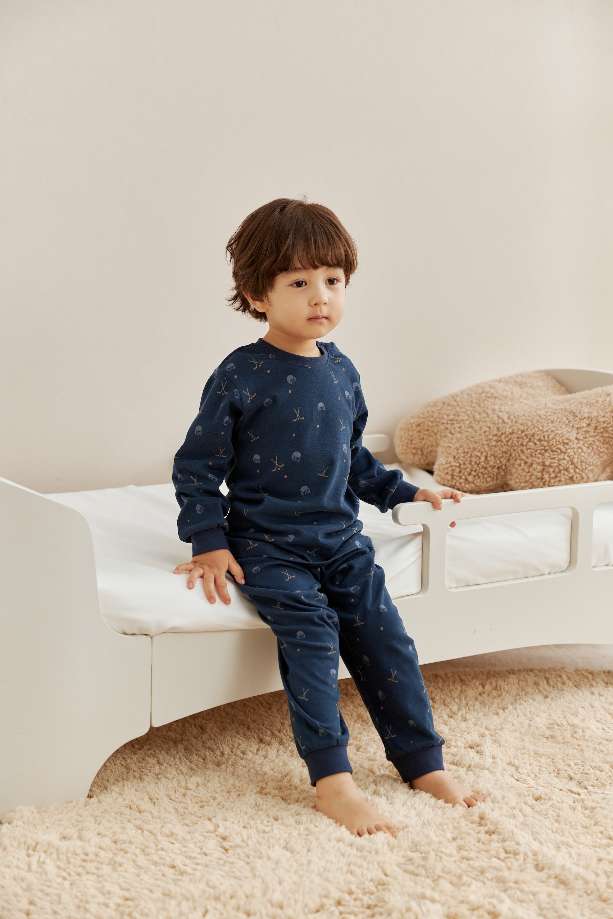 Child wearing a navy blue outfit with hockey pattern sitting on a white couch.