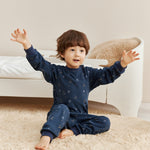 Child in navy blue pajamas sitting on a beige carpeted floor with a neutral-colored wall in the background.