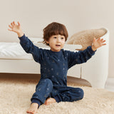 Child in navy blue pajamas sitting on a beige carpeted floor with a neutral-colored wall in the background.