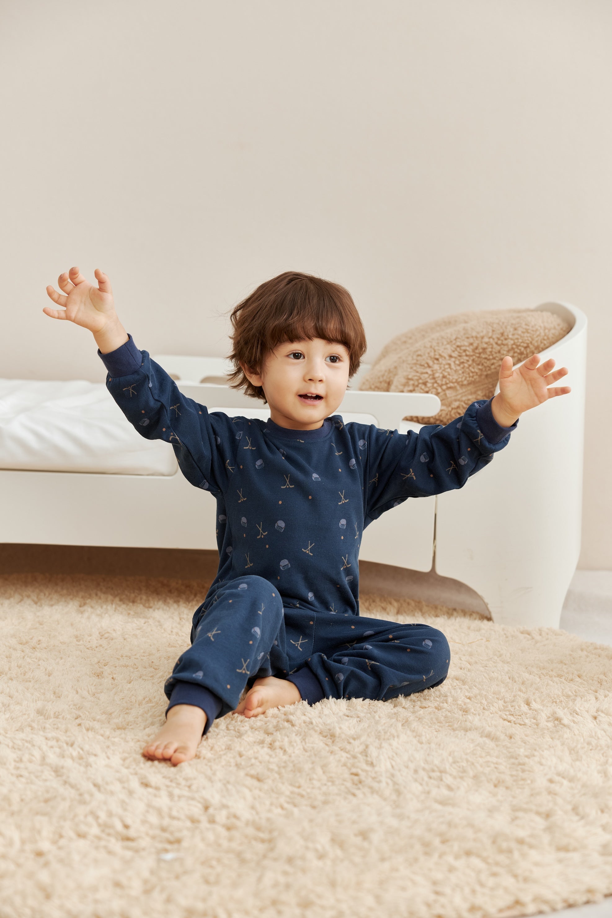 Child in navy blue pajamas sitting on a beige carpeted floor with a neutral-colored wall in the background.