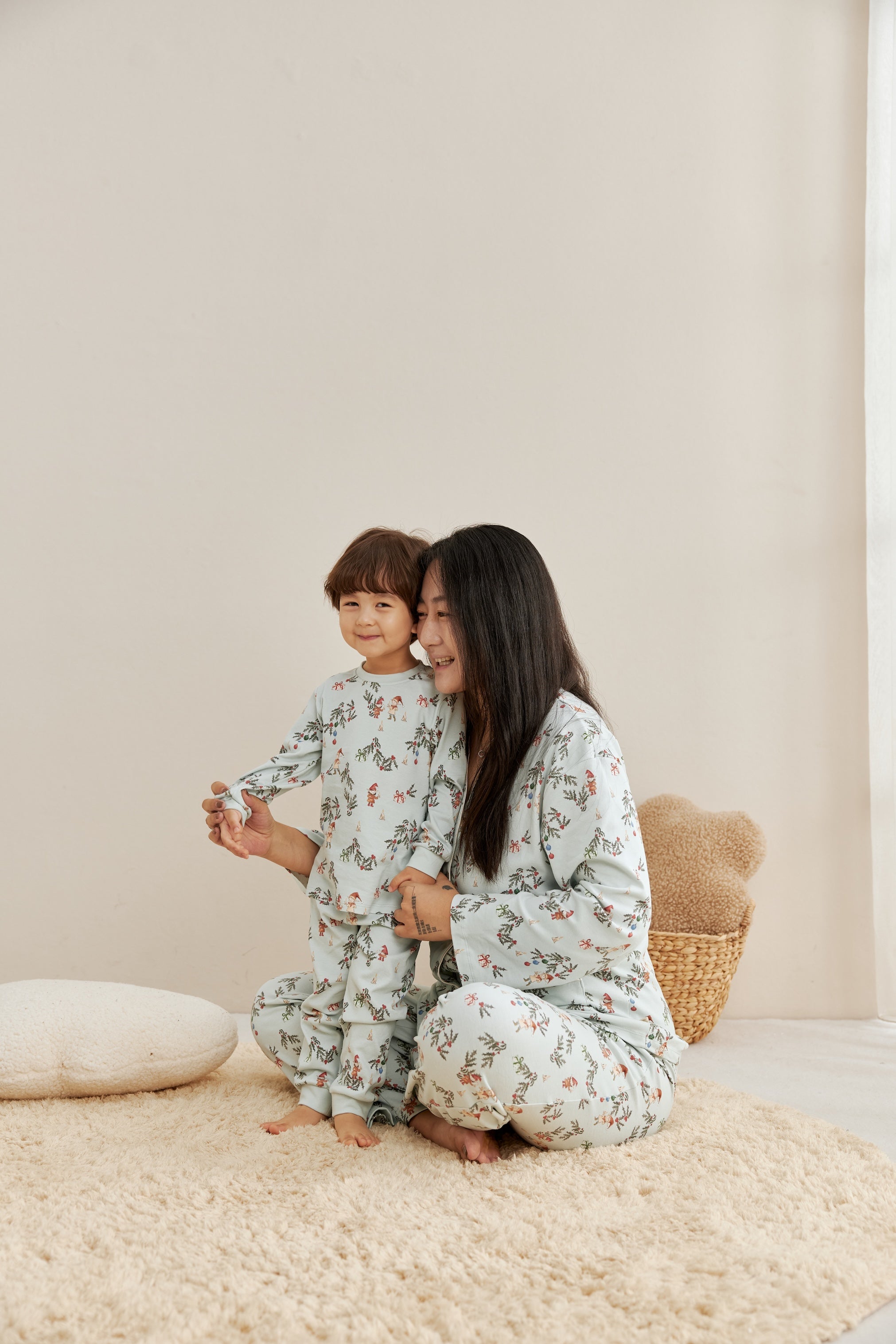 Woman and child in matching pajamas sitting on a beige rug.