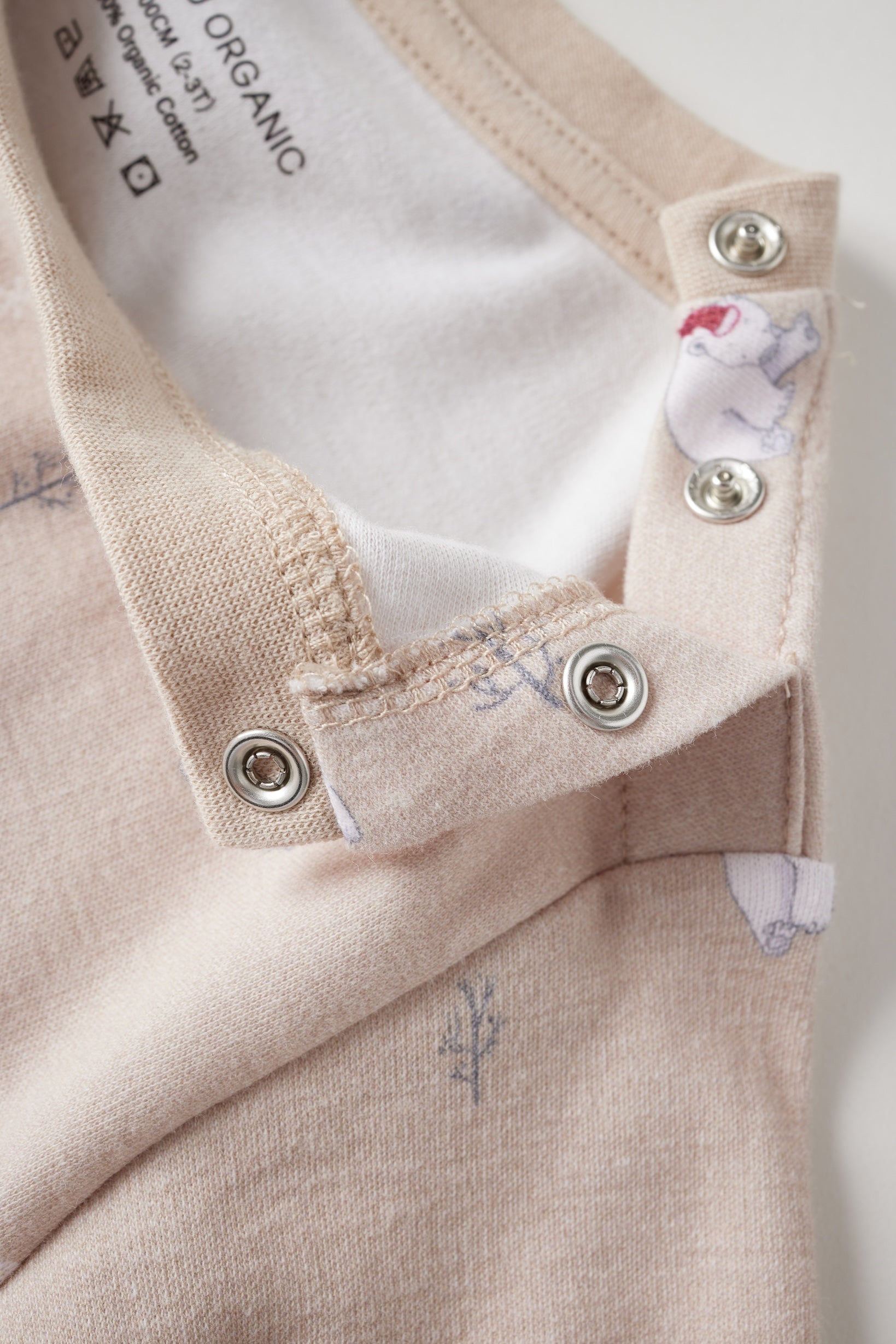 Close-up of a baby outfit with buttons and organic label on a light background