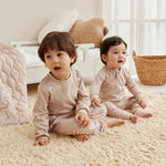 Two children sitting on a textured rug in a bright room with light-colored walls.