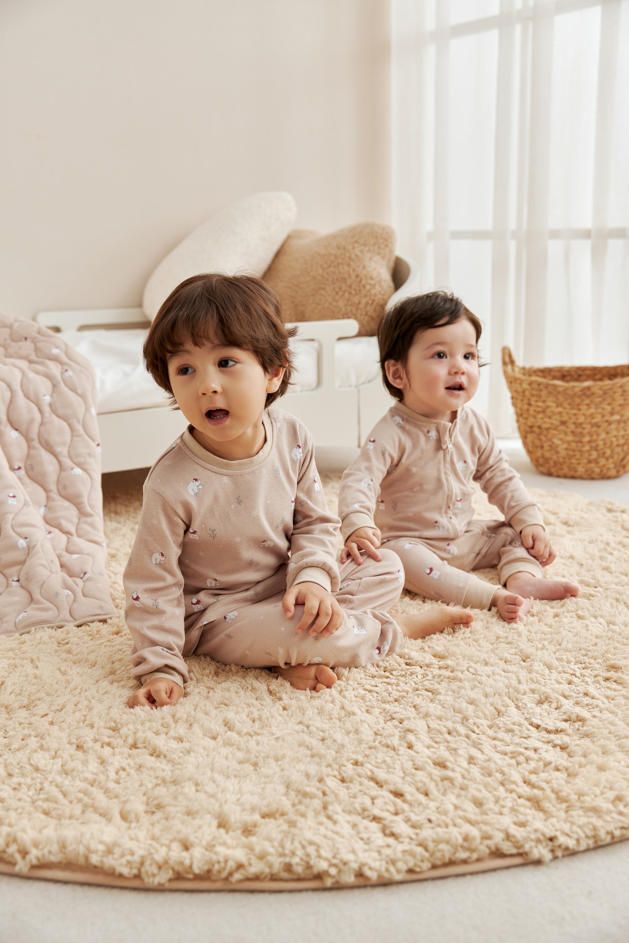 Two children sitting on a textured rug in a bright room with light-colored walls.