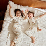 Two kids playing on a bed, one in an organic bamboo pajama set- clementine the other one in an organic zip up sleeper -clementine, embracing the spirit of bedtime fun