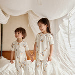 Two kids standing on a bed, one in an organic bamboo pajama set- clementine the other one in an organic zip up sleeper -clementine, embracing the spirit of bedtime fun