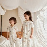 Two kids standing on a bed, one in an organic bamboo pajama set- clementine the other one in an organic zip up sleeper -clementine, embracing the spirit of bedtime fun