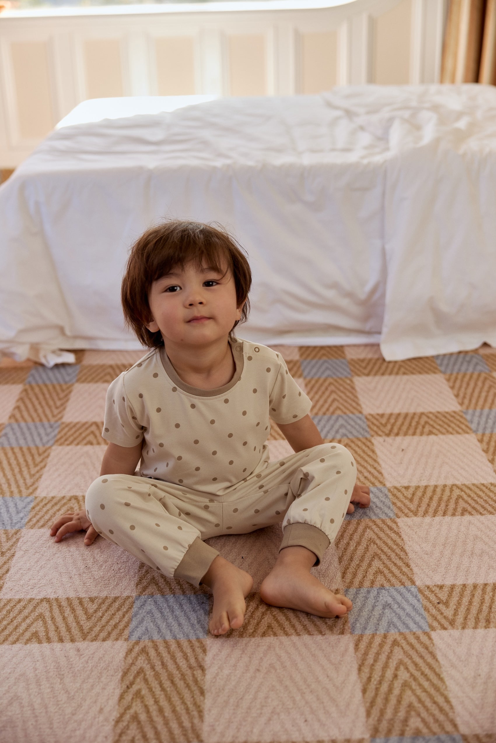 A boy in a cute dot-patterned pajama set sits on the floor