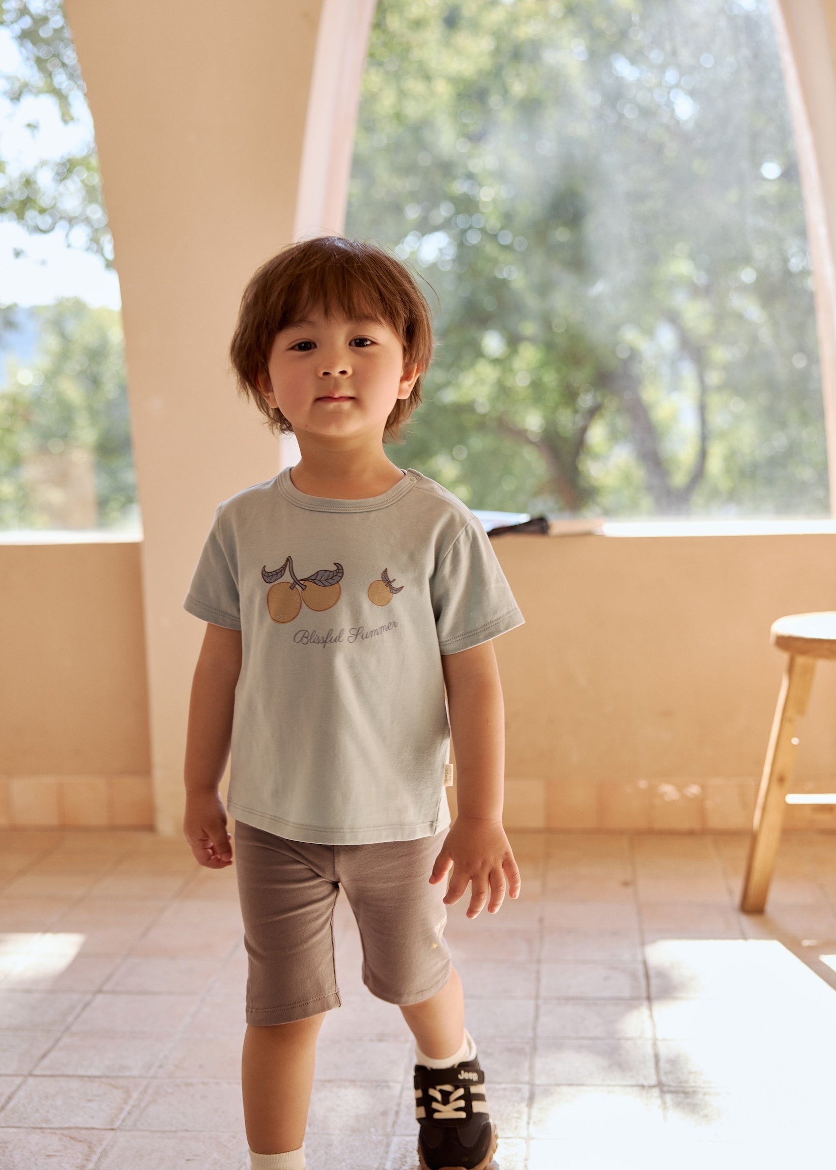 A young boy stands in a room, wearing a comfy t-shirt and ultra-soft organic toddler bike shorts