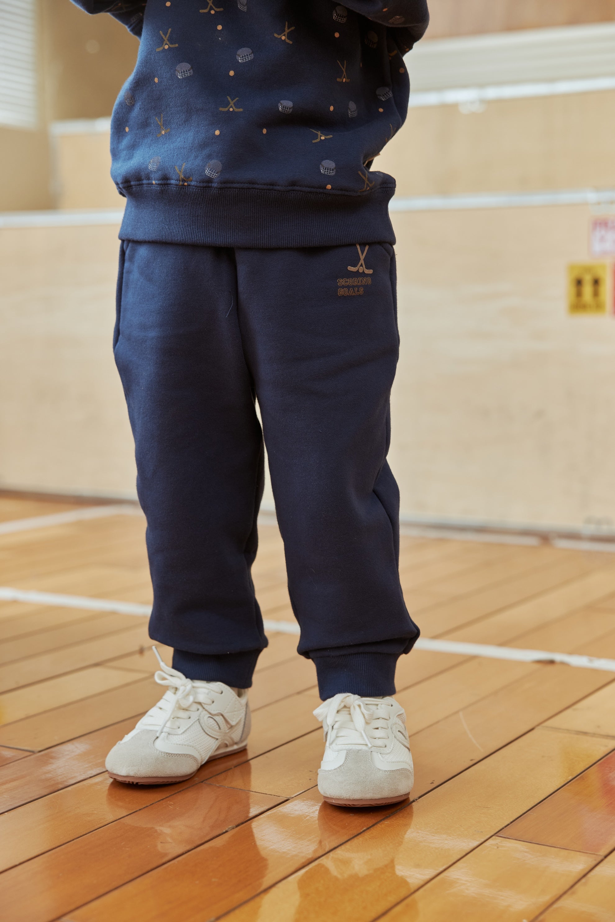 Person wearing navy blue tracksuit and white sneakers on a wooden floor.