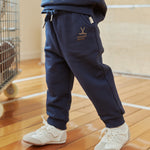 Person wearing navy tracksuit with white sneakers on a wooden floor.