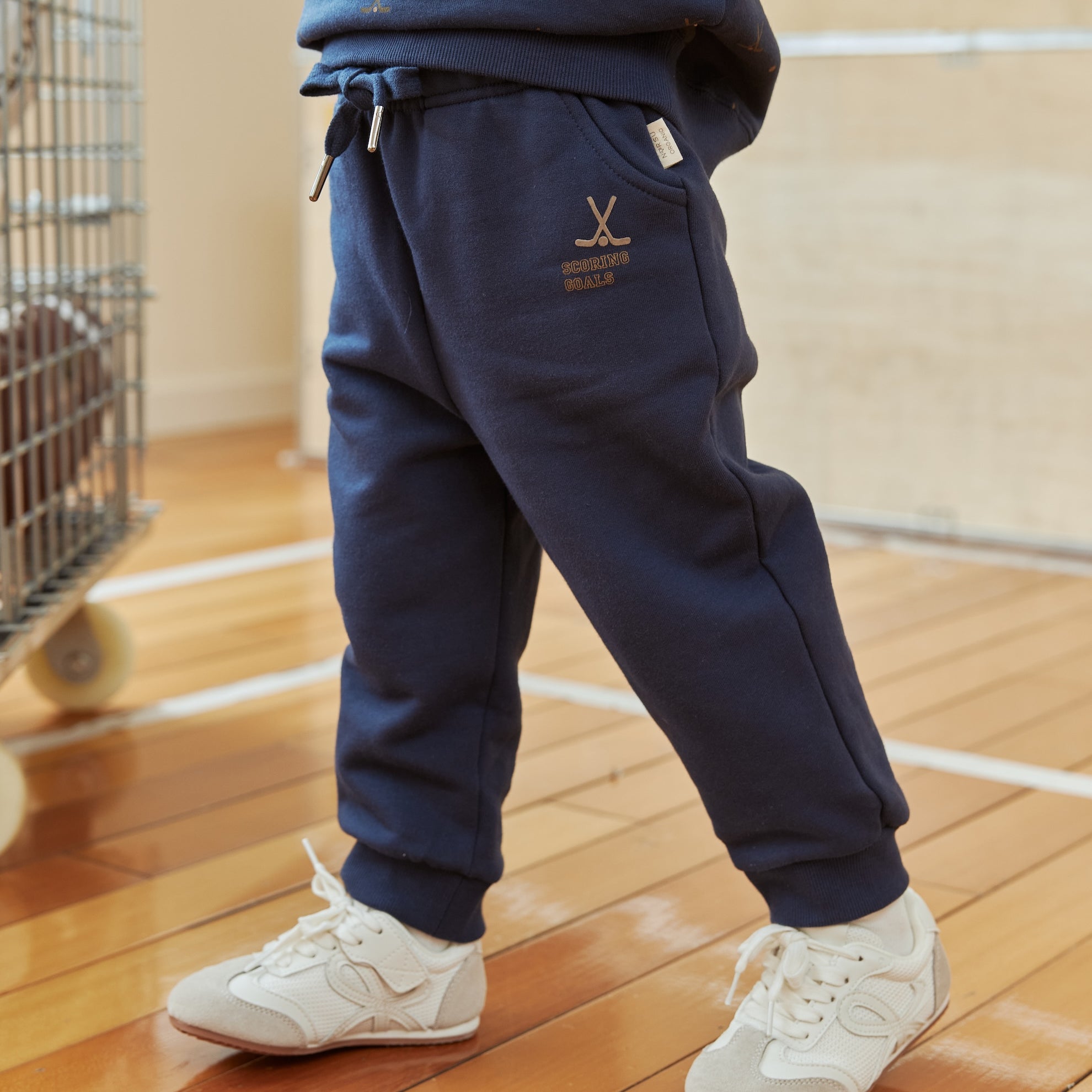 Person wearing navy tracksuit with white sneakers on a wooden floor.
