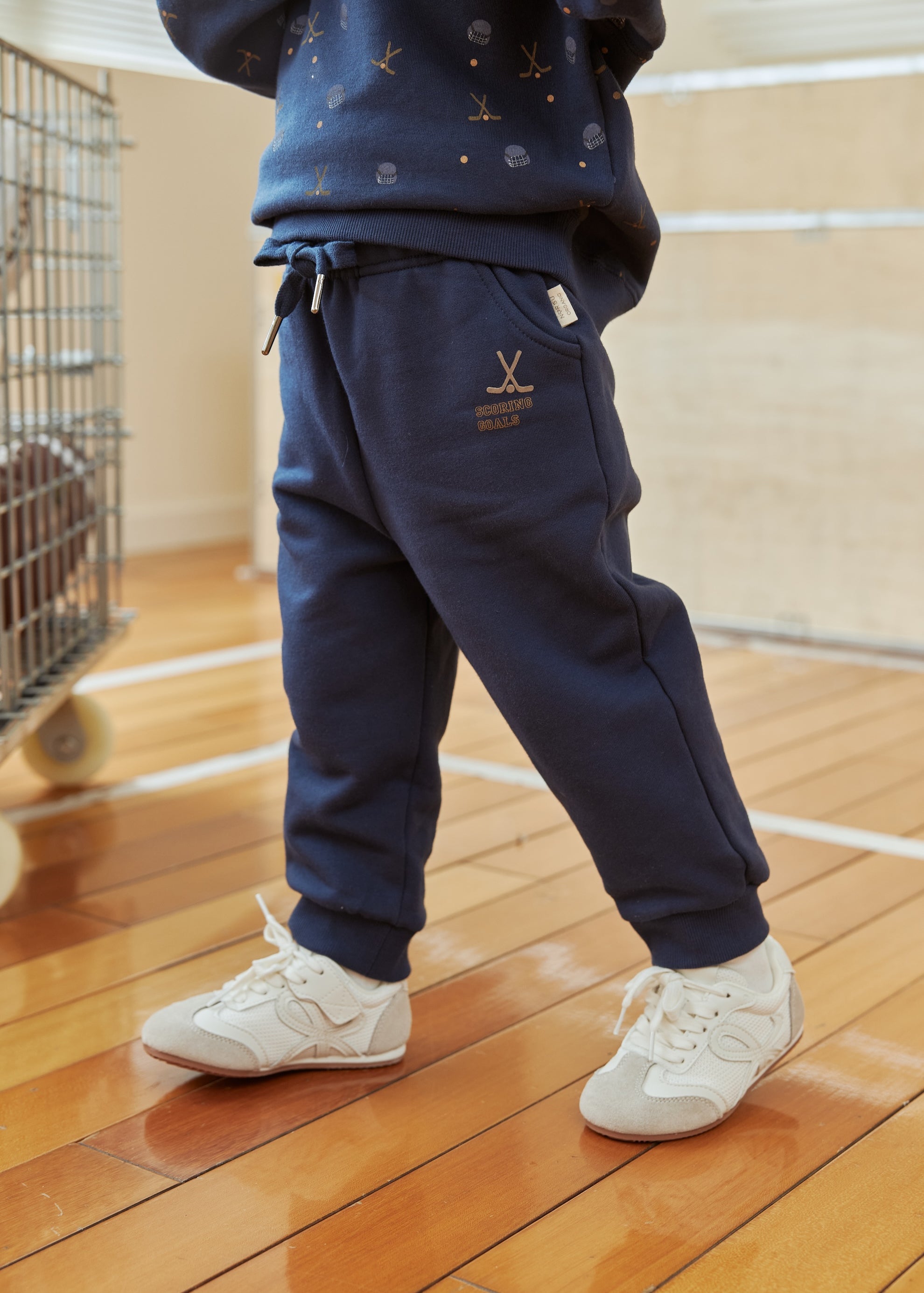 Person wearing navy tracksuit with white sneakers on a wooden floor.