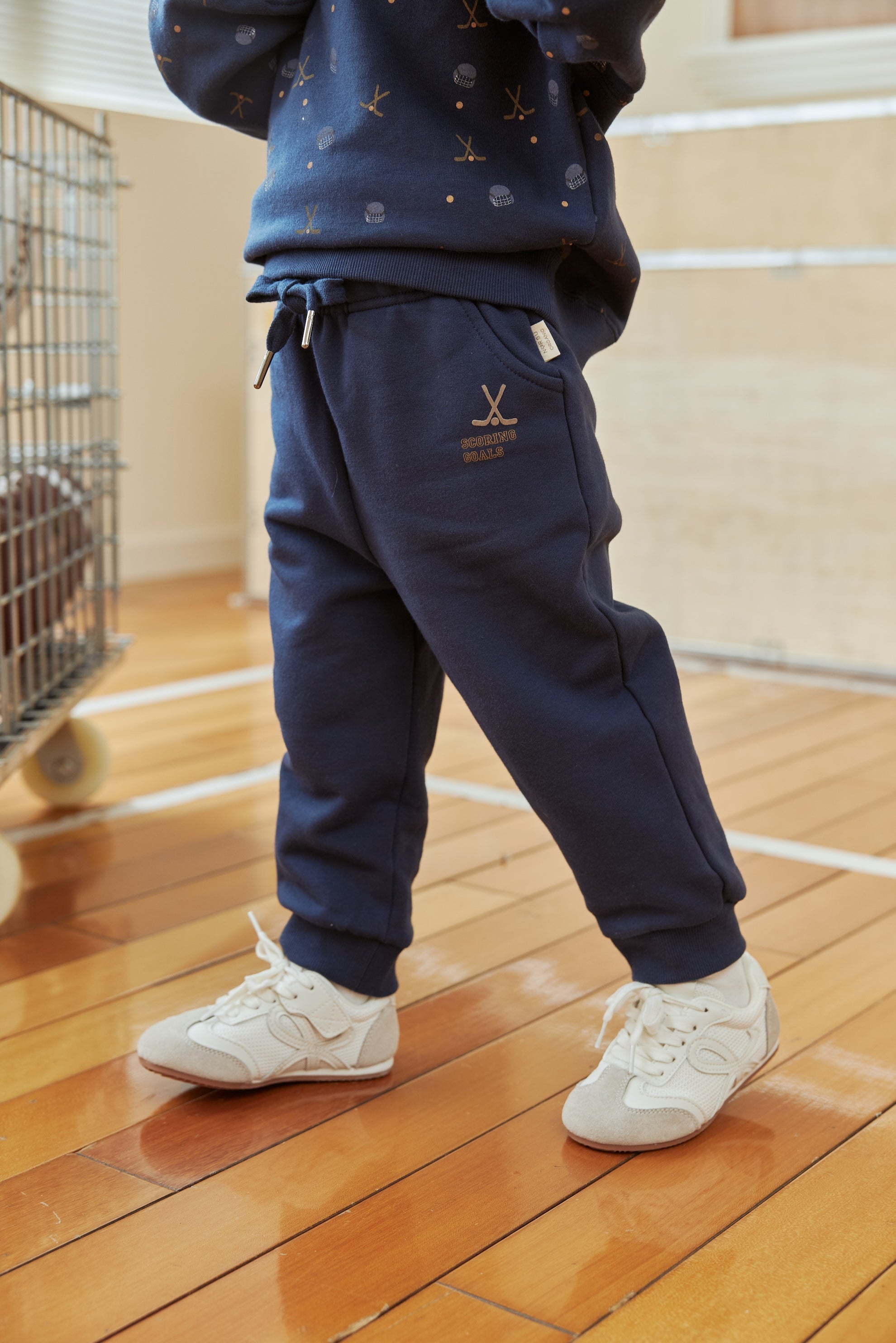Person wearing navy tracksuit with white sneakers on a wooden floor.