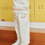 Person wearing a beige tracksuit with white sneakers in front of yellow lockers.