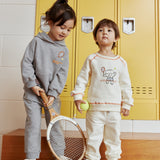 Two children in matching outfits standing in front of yellow lockers.