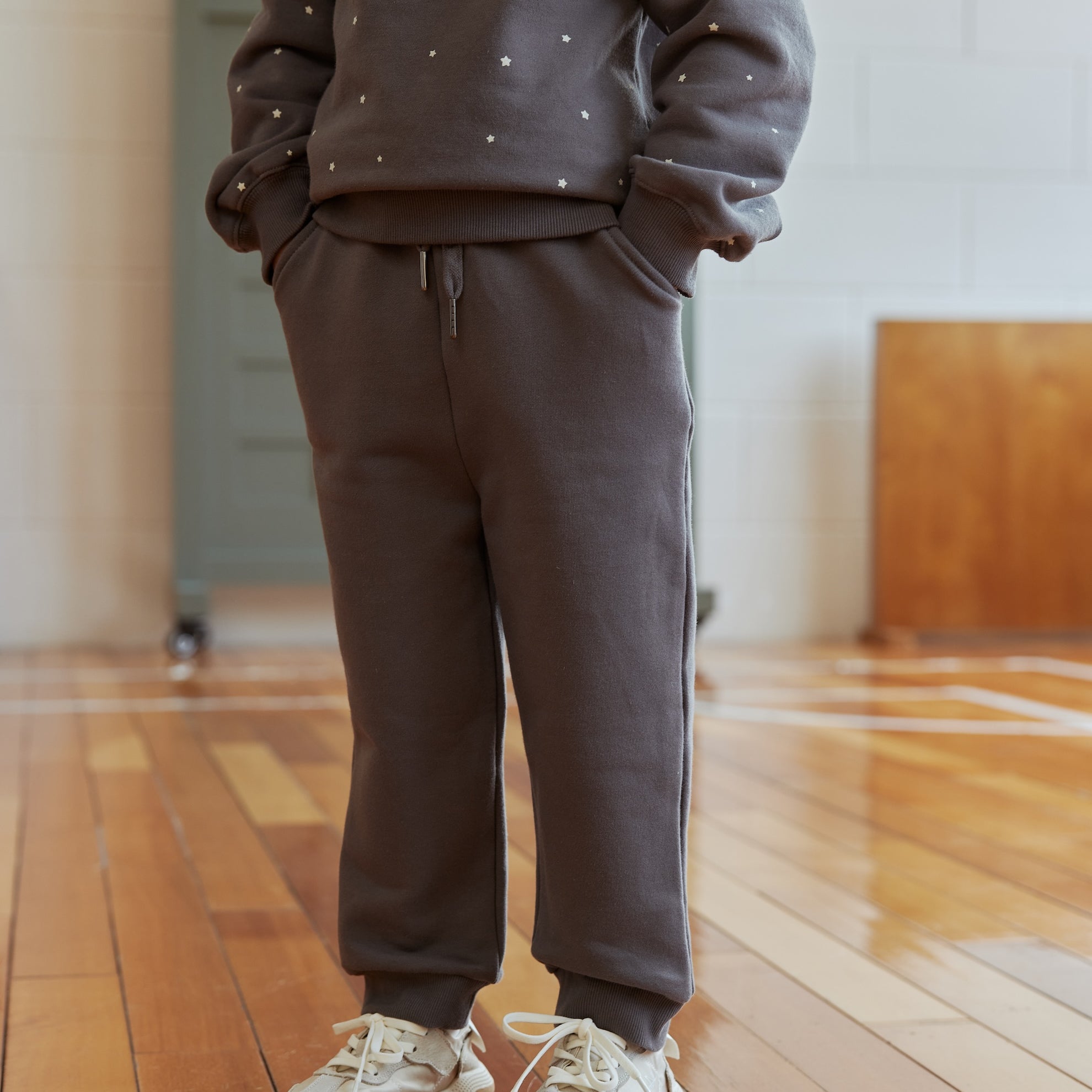 Person wearing a gray sweatshirt and pants set on a wooden floor.