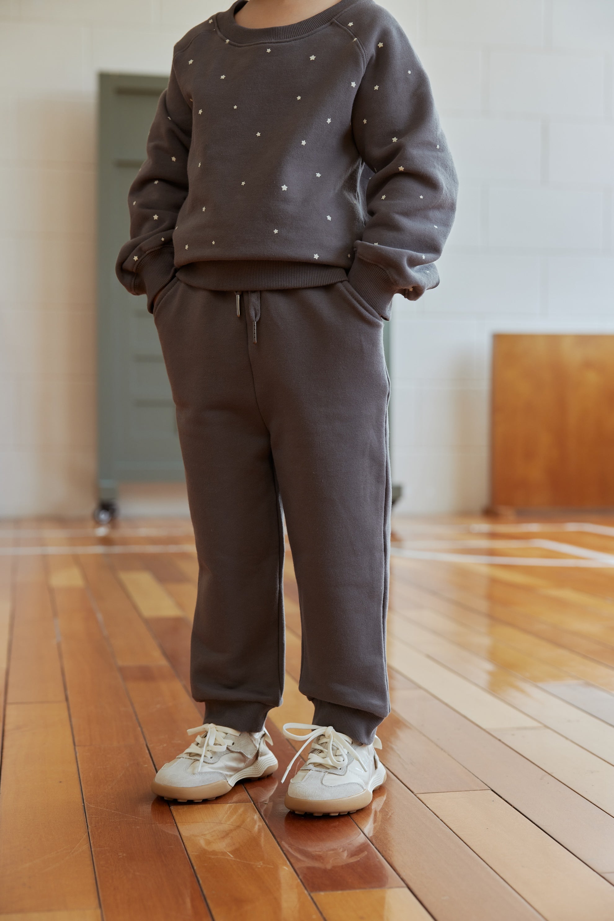 Person wearing a gray sweatshirt and pants set on a wooden floor.