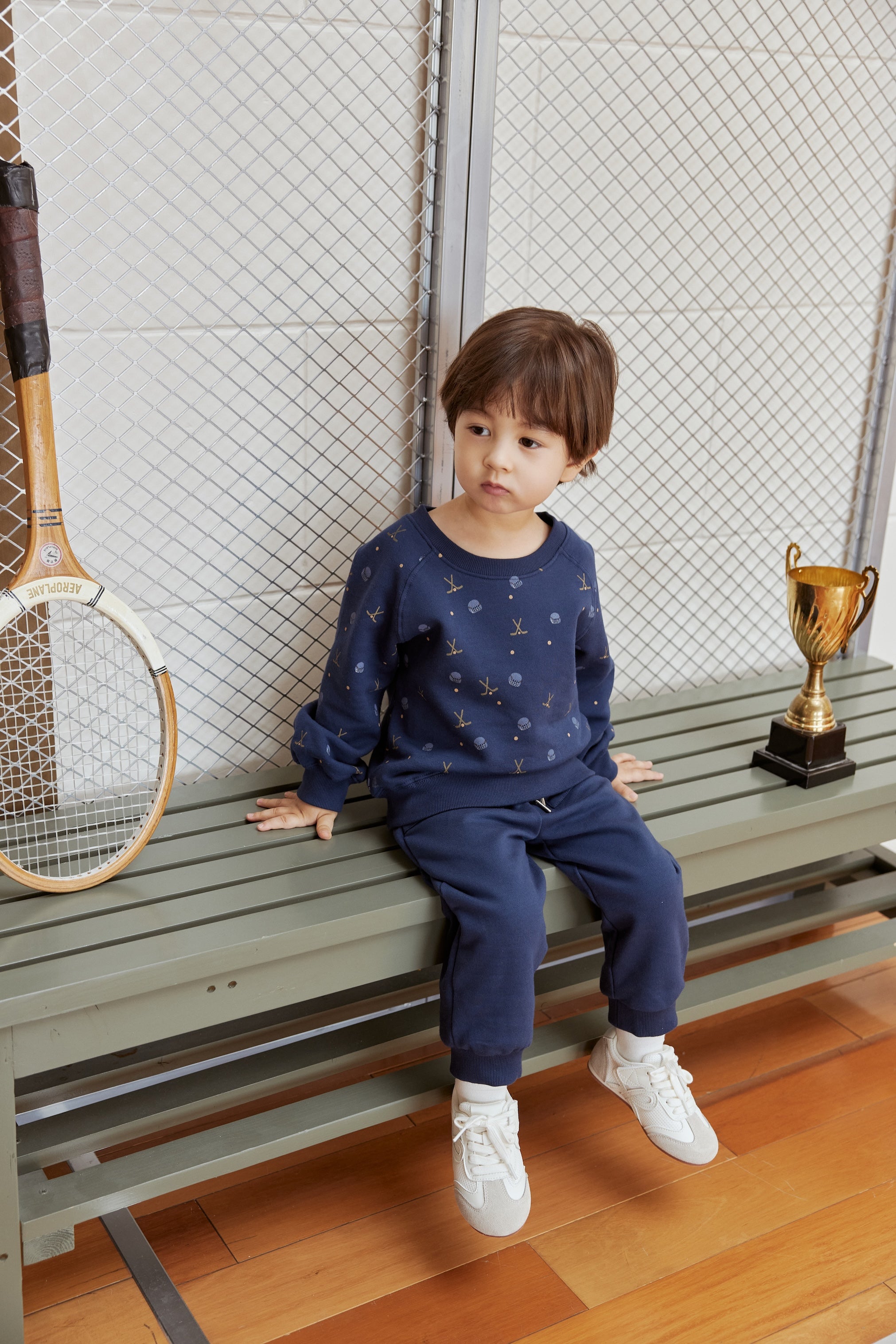 Child sitting on a bench with a tennis racket and trophy in the background