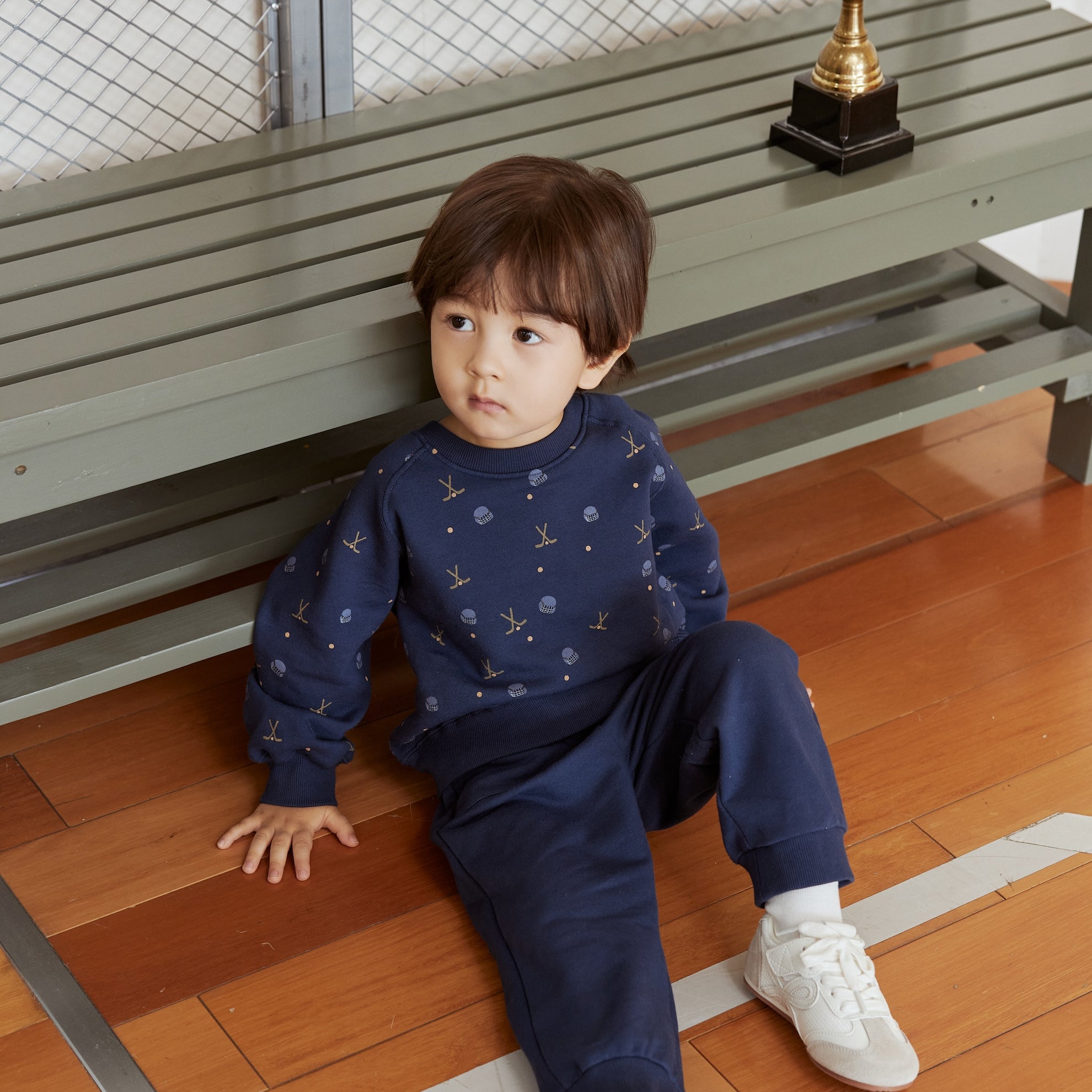 Child sitting on a wooden floor with a gold trophy in the background