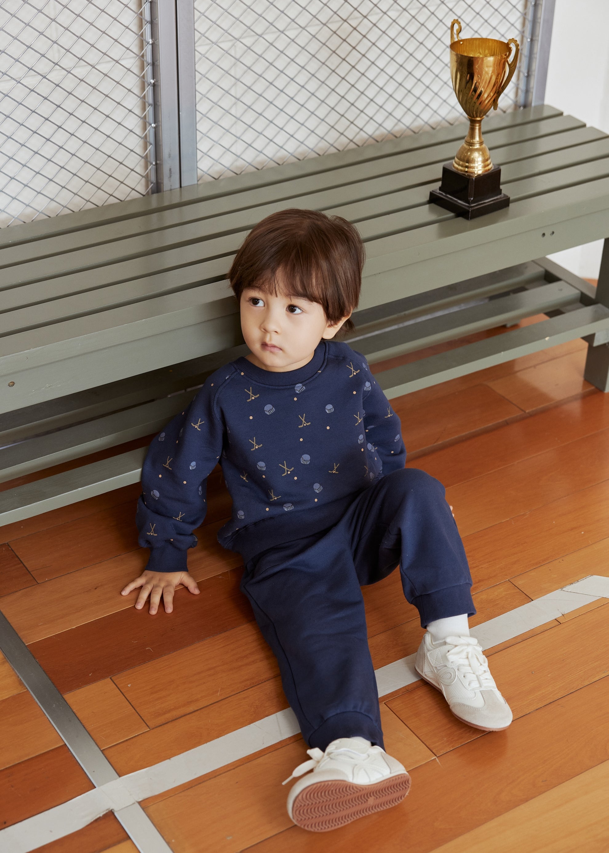Child sitting on a wooden floor with a gold trophy in the background