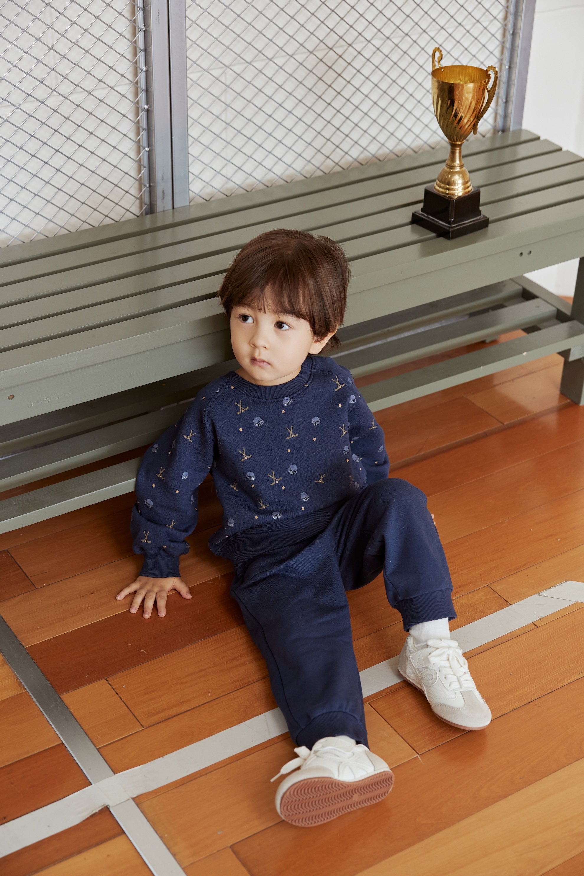 Child sitting on a wooden floor with a gold trophy in the background