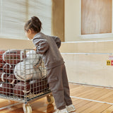 Child pushing a cart full of basketballs in an indoor setting with an emergency exit sign visible.