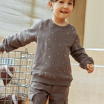 Child wearing a gray sweatshirt with white polka dots and cargo pants indoors.