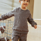 Child wearing a gray sweatshirt with white polka dots and cargo pants indoors.