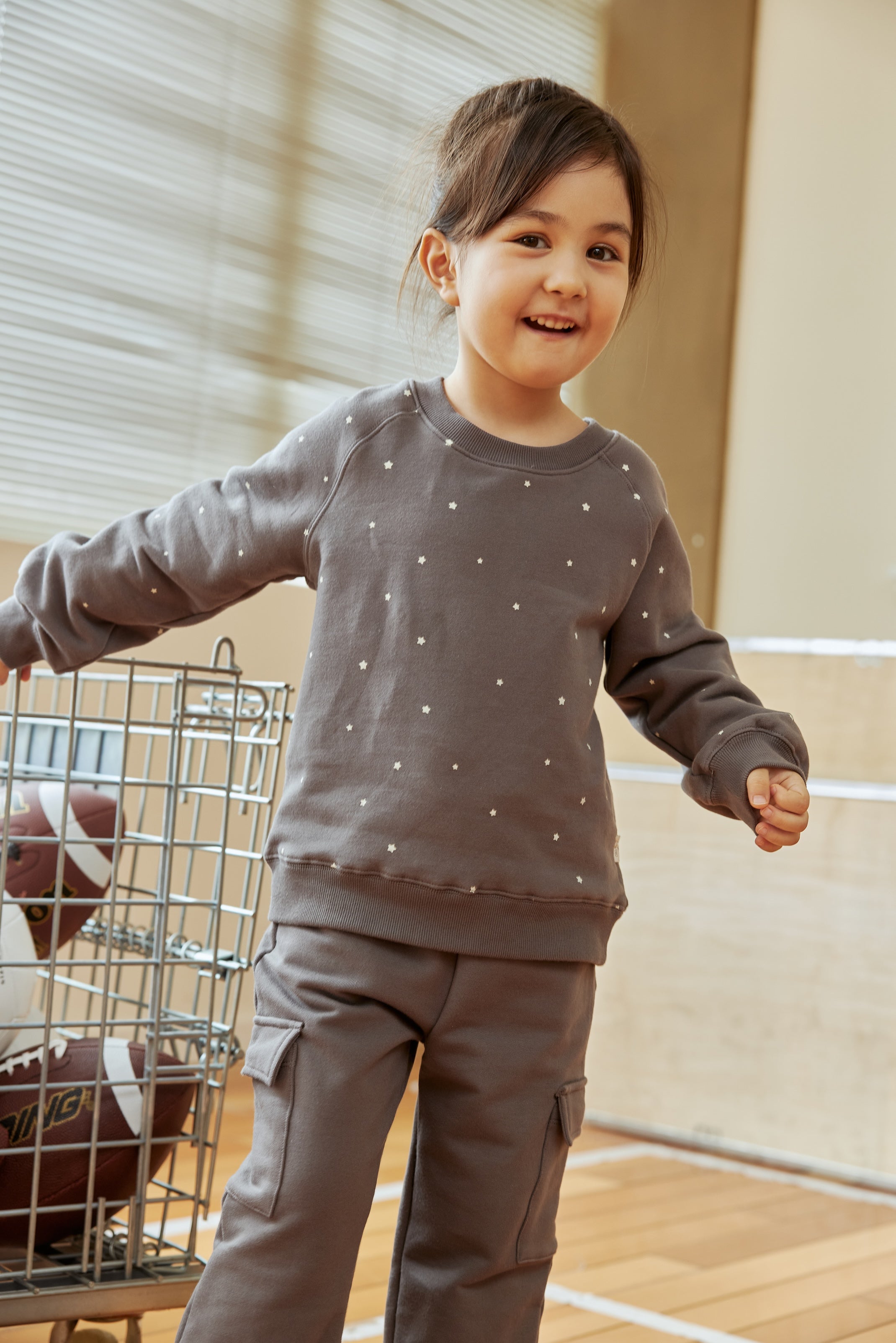 Child wearing a gray sweatshirt with white polka dots and cargo pants indoors.
