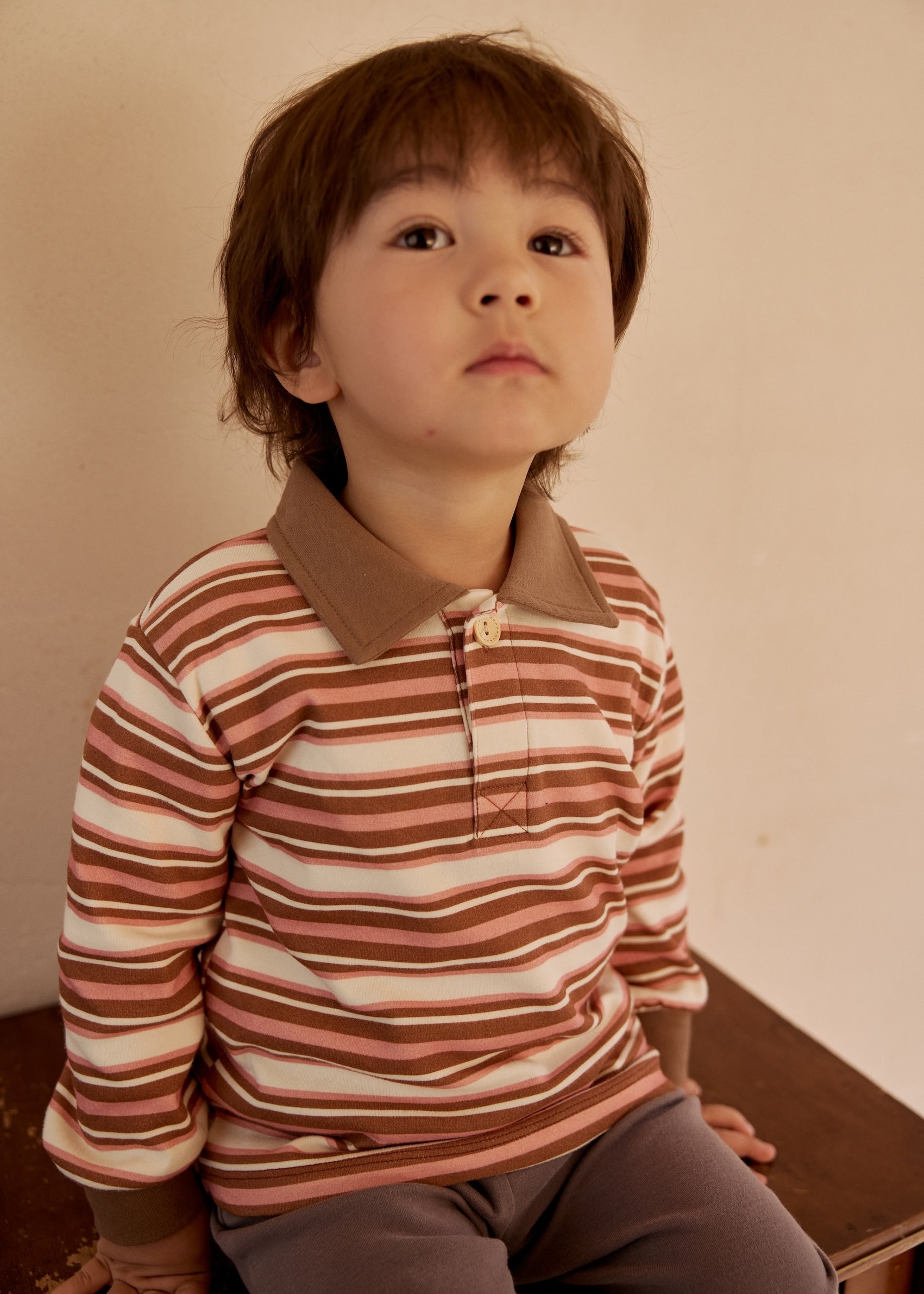 a yonge boy sit on a table and wearing Toldder Organic Polo Shirt-Brown/Pink