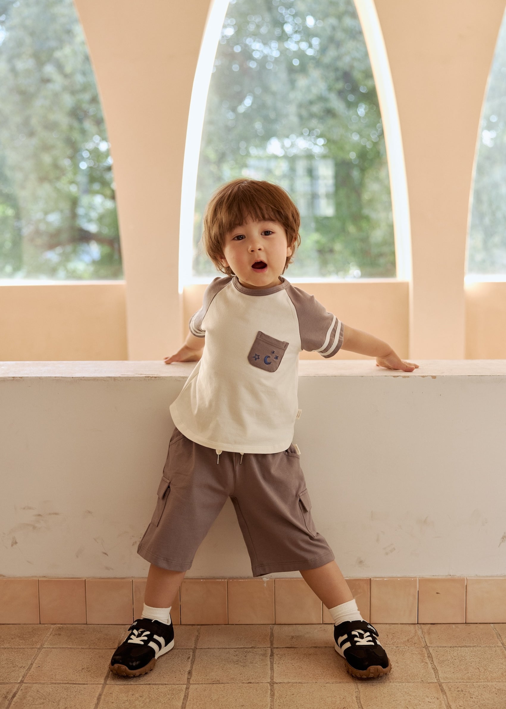 A young boy in dark grey cargo shorts stands by a sidewall, looking outside with curiosity