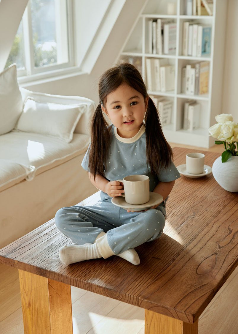 baby girl sitting and table and holding a cup of tea