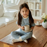 baby girl sitting and table and holding a cup of tea