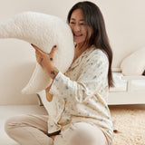 Woman sitting on a couch holding a large white pillow in a cozy living room.