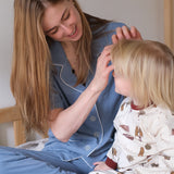 Woman and child in pajamas sitting on a bed with a book, smiling.